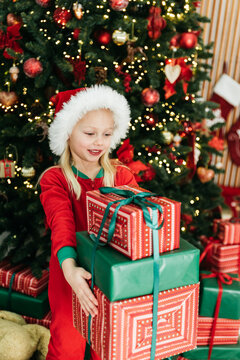 Merry Christmas and Happy Holidays. Little child under Christmas tree. baby girl in Santa Claus hat with gifts under Christmas tree with many gift boxes presents. Happy Holidays, New year.