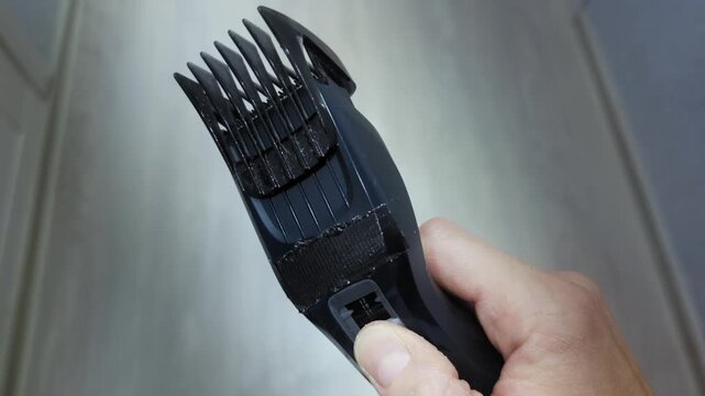 Male finger switches length setting slide of adjustable hair comb on hair clipper device. Personal grooming