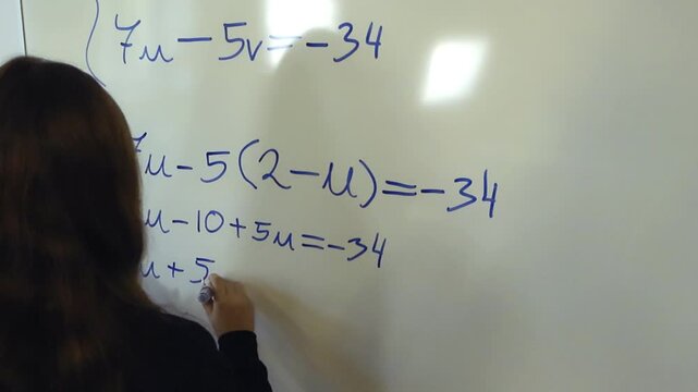 Female college student writing a complex algebra equation on a whiteboard during a math lesson in a classroom, demonstrating problem solving skills and higher education concept