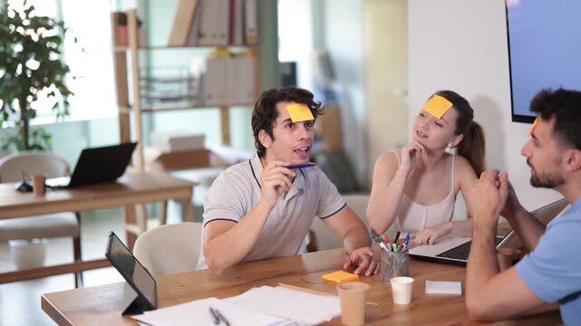 Focused young colleagues trying to guess names on forehead while spending leisure moments in office 
