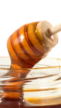 Honey drips from a wooden dipper into a clear glass jar
