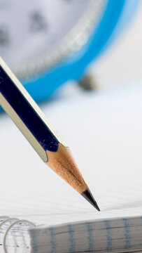 Close view of a pencil ready to write on a page beside a clock in a bright setting