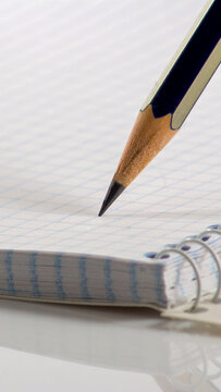 Pencil held above a spiral notebook with blank pages in a bright setting during the daytime