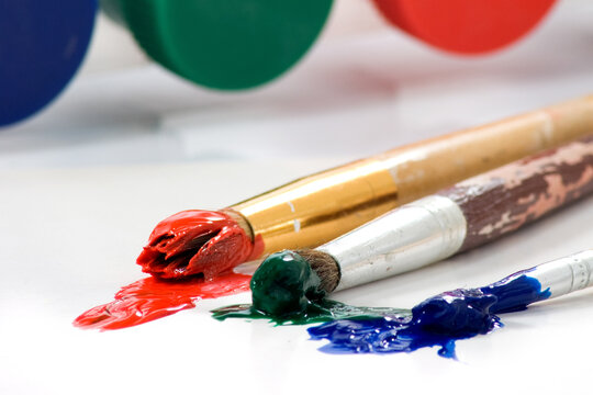 Brushes and paint are on a surface with vibrant colors at an art studio in the afternoon