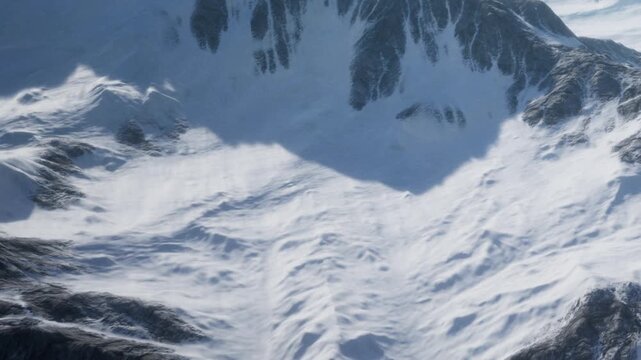 Snow covers the ground and slopes of tall mountains during daylight. Shadows fall across the terrain, creating contrast on the snow.