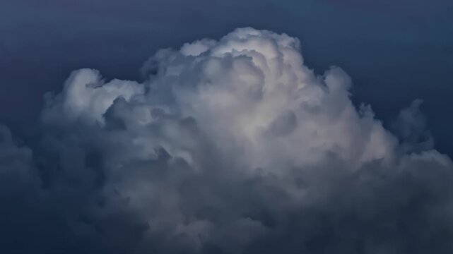 Dramatic cloud formation against dark blue sky at twilight, large atmospheric cumulus cloud with soft edges and varying shades of grey and white, vast ethereal sky background. Meteorology