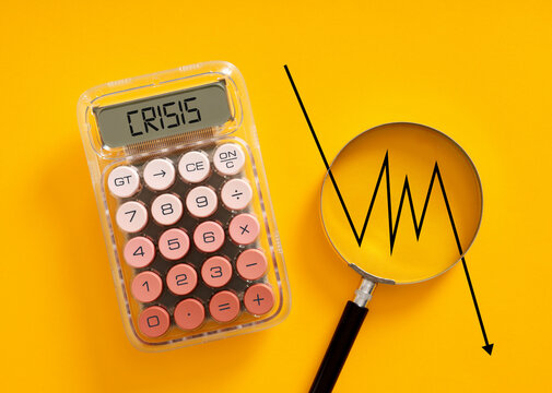 Calculator showing crisis word with falling graph on magnifying glass