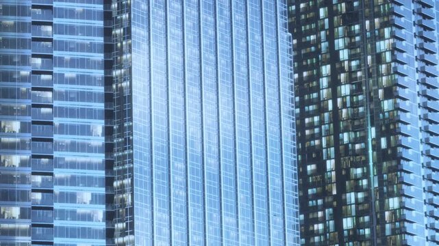 Bright lights shine from the windows of tall buildings in a city at night. The scene captures the modern structures reflecting light in an urban setting.