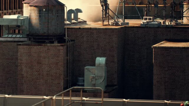 A rooftop view showing various industrial equipment and structures. Pipes and water tanks are visible on the building. The scene is set under a clear sky during the day.