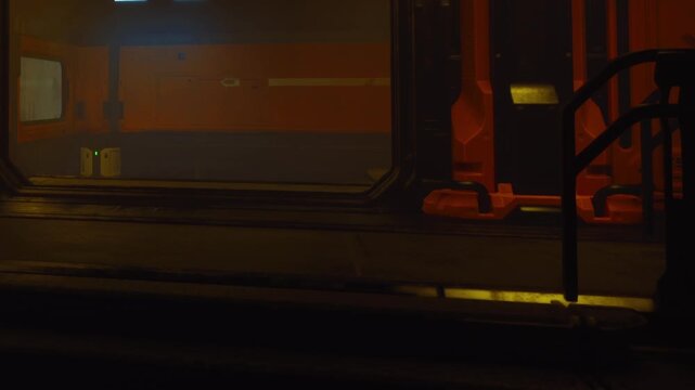 A space features dim lighting with glowing objects. The atmosphere suggests a science fiction theme. The room shows walls with red and gray colors and shadows.