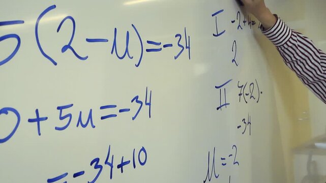 Teacher's hand wiping a blue marker off a whiteboard. Mathematical equations and formulas are being erased from the classroom board after a lesson, representing education and problem solving