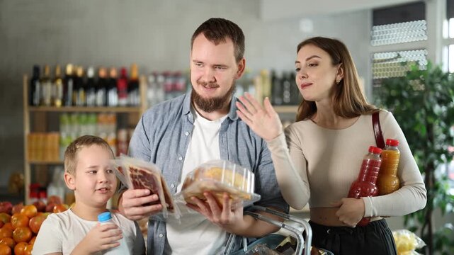 Positive young family with little son choosing some products in grocery store 