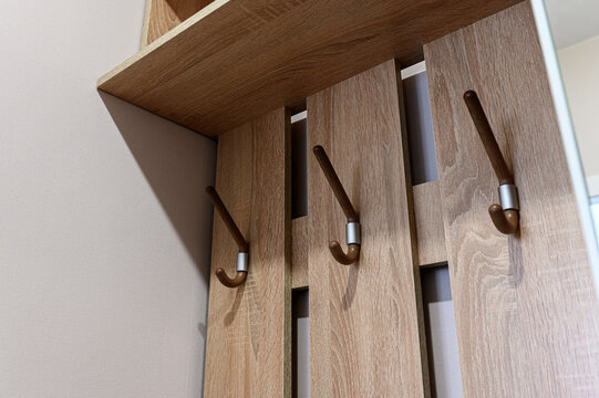 wall-mounted coat rack features light oak panels, three curved wooden hooks with silver ferrules,  matching overhead shelf for compact, functional entryway solution