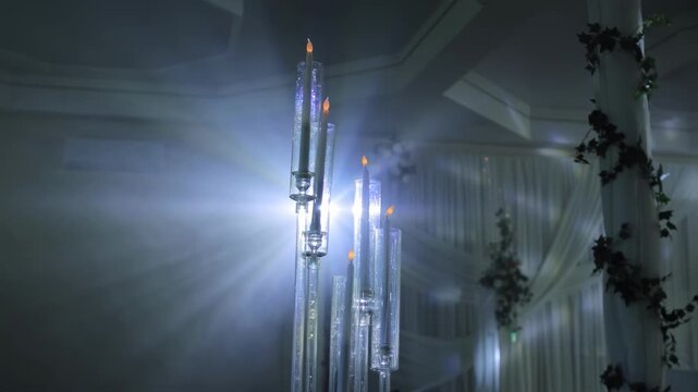 Illuminated elegant candle holders with flickering lights provide warm and romantic ambiance in a luxurious indoor event space, featuring bright lens flare and starburst effect slow motion