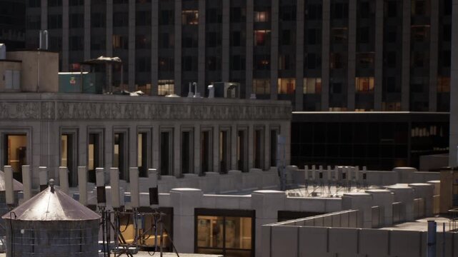 The scene shows rooftops of several buildings in a city. There are water towers and chimney structures. Windows of nearby buildings reflect daylight.
