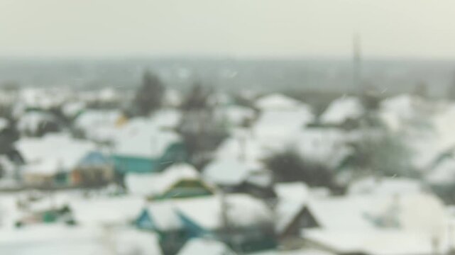 Abstract blurred focus winter landscape of snow covered rooftops of numerous village houses with light snowfall outdoor during daytime, slow mo