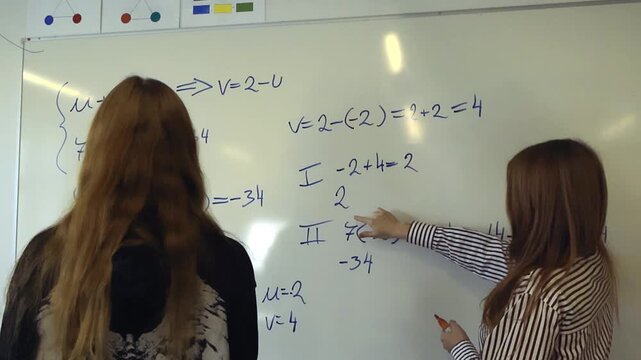 Young female teacher explaining a difficult math problem on a whiteboard to her student during a lesson. Private tutoring and individual learning concept with two people in a classroom