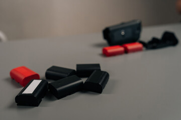 Naklejka premium Camera digital system with power supply accessory and multiple charged, discharged red and black lithium-ion rechargeable battery packs for professional photography equipment, close-up, cropped shot.