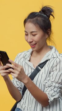 Vertical Screen : Happy Asia youth casual girl smile enjoy typing smartphone message with friend stand over isolate yellow empty space background., Hands device chat online advertise. Face expression.