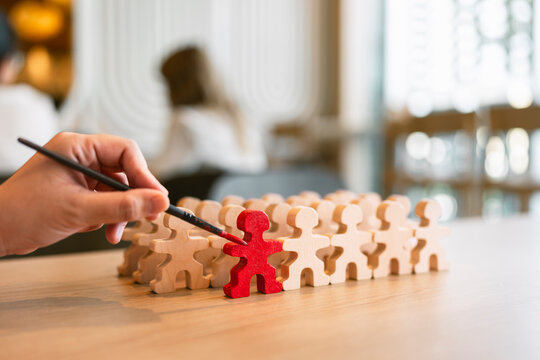 Talent recruitment and leadership concept with hand painting wooden figure in red among crowd on table for employee selection, career training, standout candidate and business development.