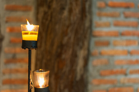 Candlelight and cozy ambiance concept with burning yellow candle in glass holder on rustic metal stand against brick wall for spa meditation, memorial vigil and romantic dinner lighting.