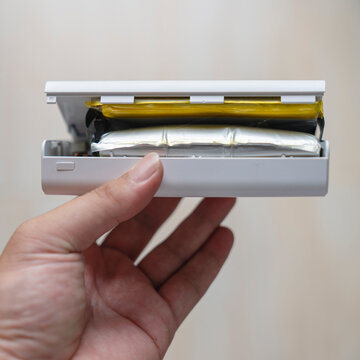 Damaged electronics and battery safety concept with hand holding swollen power bank with cracked plastic case showing dangerous bloated lithium cell for hardware repair and waste recycling.