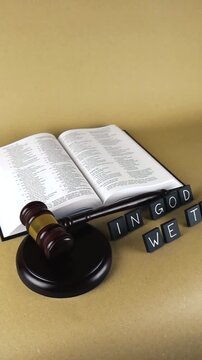 Open holy bible resting on a brown background next to a judge's gavel and the national motto of the United States, representing the intersection of law, faith, and American values
