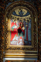 Naklejka premium Ancient orthodox icon of angels in golden frame. Old Christian icon depicting archangels and saints with halos surrounded by ornate gilded baroque frame with hanging metal incense burner lamp
