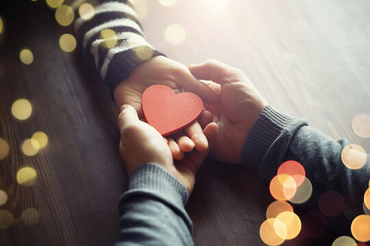 Woman holding hands with red heart on wooden background, top view