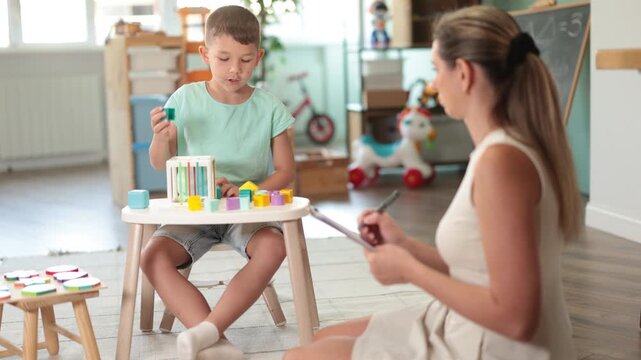 Child psychologist conducts test - asks boy to insert figures of different shapes and colors into a cube. High quality 4k footage