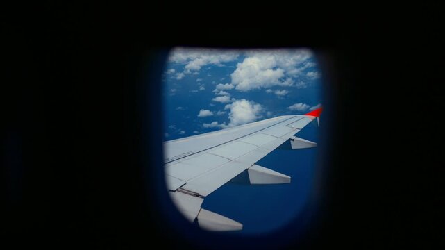 View from passenger seat through airplane porthole, plane wing and white clouds. Flight by plane, contemporary airlines service for traveling and business trip, beautiful view on sky and cloudscape