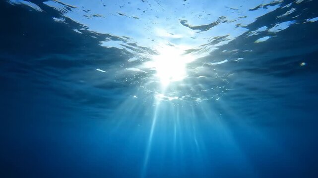 Underwater view with bright sun rays piercing through blue ocean surface, natural light and serene atmosphere