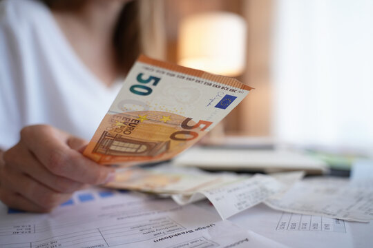 Woman counting euro banknotes while looking over bills and receipts at home
