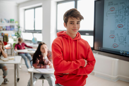 Portrait of confident teenage student standing in high school classroom.