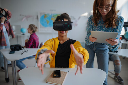Teacher guiding teenage student using virtual reality technology at school.