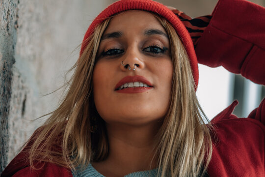 A stylish woman wearing a red hat and coat is posing against a gray wall.