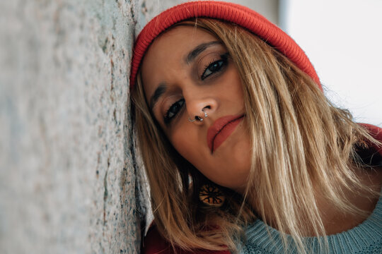 A stylish woman wearing a red hat and coat is posing against a gray wall.
