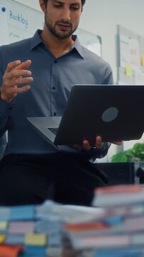 Vertical Screen : Thoughtful young Latin businessman stand with laptop analyzing data paperwork stack. Hybrid work, digital transformation strategy, business corporate finance, executive decision.
