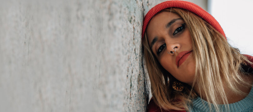 A stylish woman wearing a red hat and coat is posing against a gray wall.