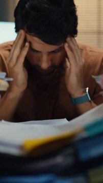 Vertical Screen : Stressed young Latin businessman having severe headache and migraine in night office. Debt crisis, corporate burnout, late overtime workload, mental health anxiety, business failure.
