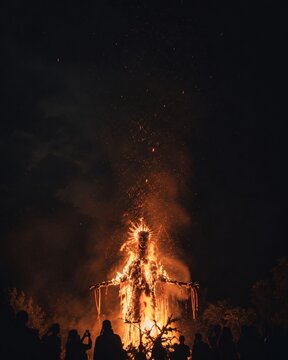 Silhouette of crowd watching giant wooden effigy burning at night