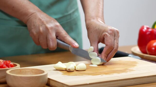 Hands chopping fresh garlic with a kitchen knife for homemade cooking.