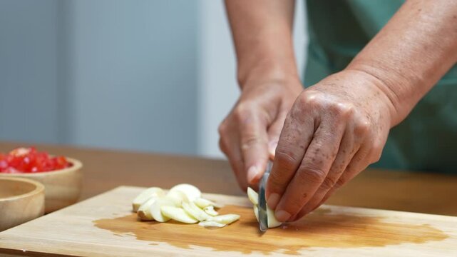 Hands chopping fresh garlic with a kitchen knife for homemade cooking.