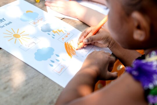 Child coloring a weather chart with crayons at a table outdoors.