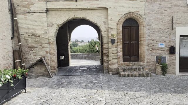 Antico borgo storico italiano, caratterizzato da un grande arco in pietra che si apre su un panorama rurale.