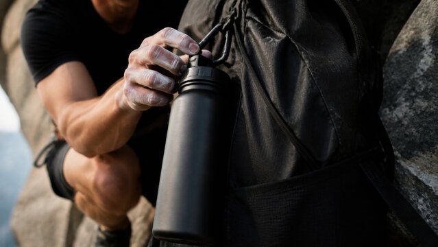 Hiker attaching a water bottle to a backpack during an outdoor adventure. Close-up of essential hiking gear, travel preparation and active lifestyle in nature.