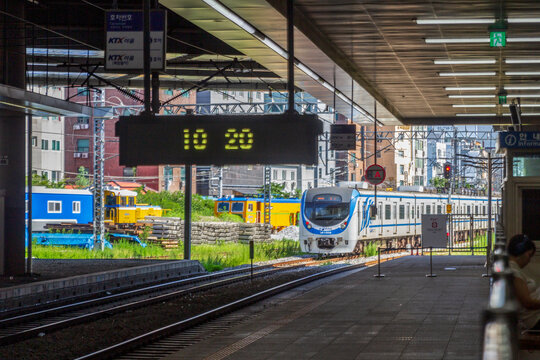 Multiple commuter trains stand beside parallel tracks and platforms beneath a large station canopy with urban buildings in the background.