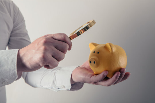 Man holding a piggy bank and a magnifying glass in his hand