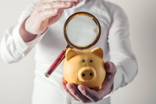 Man holding a piggy bank and a magnifying glass in his hand