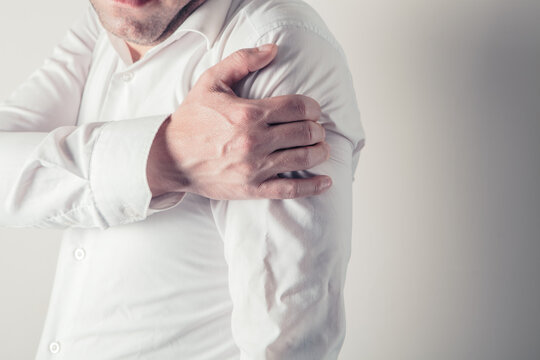 Man in white shirt suffering from pain in shoulder, close-up